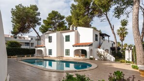 A modern villa with a swimming pool, surrounded by lush greenery and trees. - APARTAMENTO FONA (Cala Blanca)