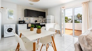 A modern kitchen with white cabinets, a dining area with a table and chairs, and a balcony with a view. - APARTAMENTO FONA (Cala Blanca)