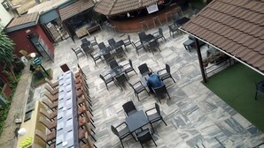 A terrace with multiple tables and chairs, a long dining table with chairs, and a small building with a tiled roof. - Davies Hotels  (Ibadan)