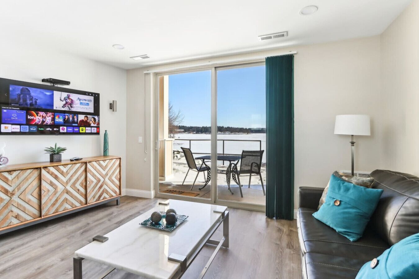Ein modernes Wohnzimmer mit Flachbildfernseher, Couchtisch, Sofa und einem Balkon mit Sitzgelegenheit.