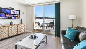 A modern living room with a flat-screen TV, a coffee table, a sofa, and a balcony with outdoor seating.