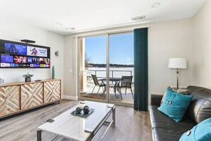 Una sala de estar moderna con una televisión de pantalla plana, una mesa de centro, un sofá y un balcón con mobiliario exterior.