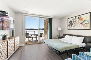 Habitación de hotel moderna con una cama grande, un escritorio y un balcón con vistas al agua.