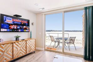 A modern living room with a flat-screen TV displaying a winter alert, a wooden cabinet, and a view of a snowy landscape through large sliding glass doors. - Luxury Beachfront Retreat at Delton Grand (Wisconsin Dells)