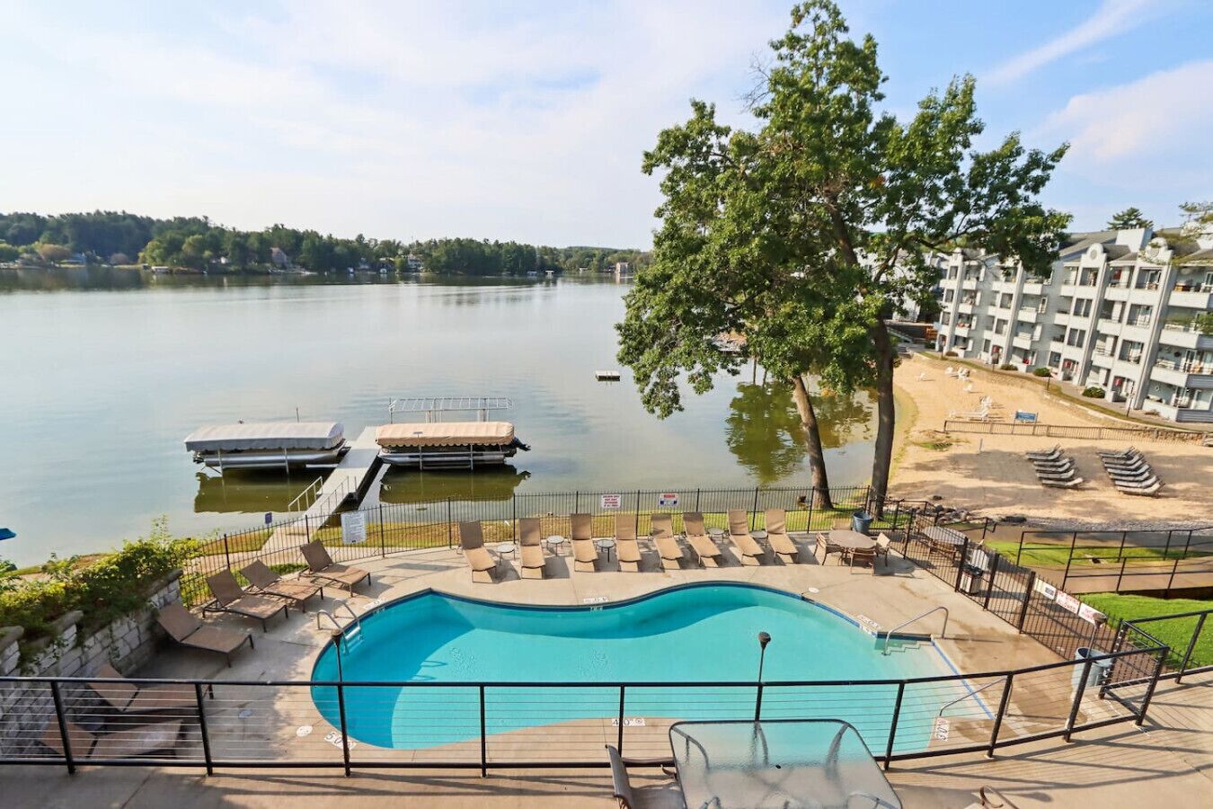 A swimming pool with lounge chairs, a dock, and a view of a lake and buildings in the background.