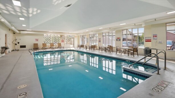 Ein großer, überdachter Pool mit freier Sicht auf das Pool-Areal, inklusive einer Sitzgelegenheit am Pool und einem Rettungsschwimmerstand.