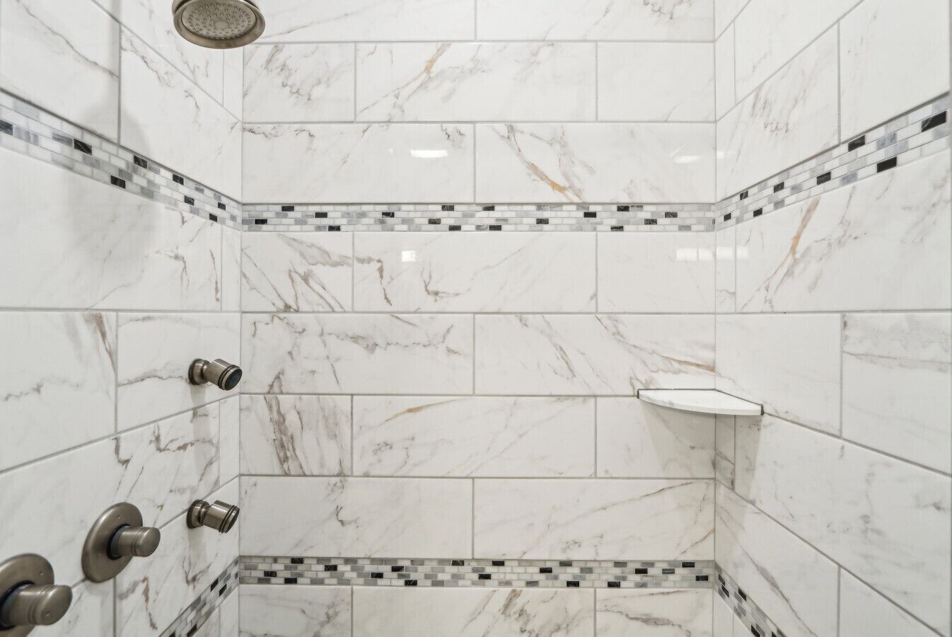 A corner shower with white marble tiles and a mosaic border.