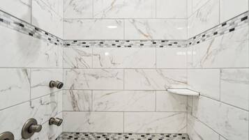 A corner shower with white marble tiles and a mosaic border.