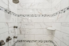 Ducha en esquina con azulejos de mármol blanco y un borde de mosaico.