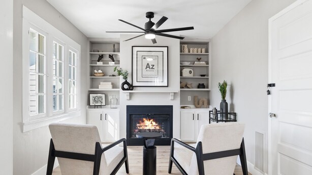 A living room with a fireplace, two armchairs, a coffee table, and a ceiling fan.