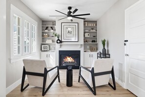 A living room with a fireplace, two armchairs, a coffee table, and a ceiling fan.