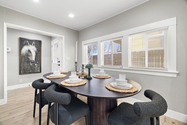 A dining area with a round table, six chairs, and a painting on the wall.