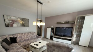 Una sala de estar moderna con un sofá seccional, una mesa de centro, un televisor y un mueble con puertas de cristal.