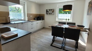 Una cocina moderna con una isla central, un comedor con mesa y sillas, y vistas a zonas verdes.