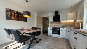 Una cocina moderna con comedor, que incluye una mesa de madera, sillas negras y una lámpara colgante.