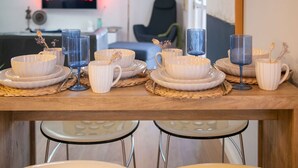 A dining area with a wooden table set with white plates, bowls, and striped cups, accompanied by blue glasses.