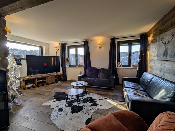 A cozy living room with a flat-screen TV, leather sofas, a cowhide rug, and a wooden ceiling.