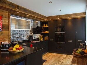 A modern kitchen with dark cabinetry, a wooden ceiling, and patterned backsplash.