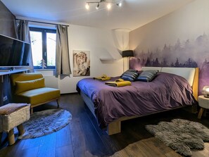 A bedroom with a bed, a chair, a TV, and a painting on the wall.