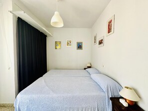 A bedroom with a bed, a hanging light fixture, a nightstand with a lamp, and three framed pictures on the wall.