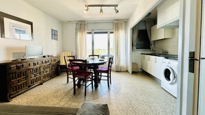 Ein kompakter Wohnraum mit Esstisch, Stühlen, einer Couch, einem Fernseher, einer Waschmaschine und einer Küchenzeile.