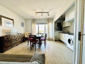 A compact living space with a dining table, chairs, a sofa, a TV, a washing machine, and a kitchenette.