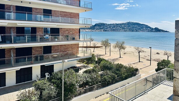 Ein mehrstöckiges Gebäude mit Balkonen, das auf einen Strand und eine entfernte Hügelkette blickt.