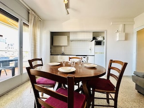 A dining area with a round wooden table, four chairs, and a view of the city through large windows.