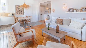 A bright, white interior with a wooden floor, a dining area with a table and chairs, a white sofa with cushions, and a coffee table with a vase.
