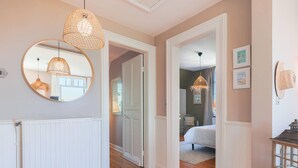 A hallway with wooden flooring, a mirror, and a wicker pendant light.