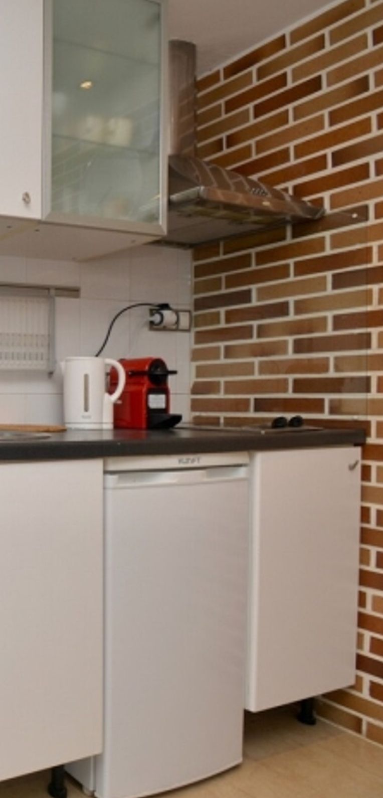Een kleine keuken met witte kastjes, een koffiezetapparaat en een vaatwasser.