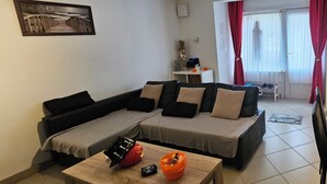 A living room with a sectional sofa, a coffee table, and a small table with decorative items. - Quiet and relaxing apartment in Coxyde, 5 minutes walk from the beach (Koksijde)