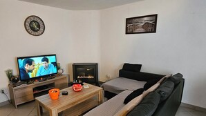 A living room with a sofa, a coffee table, a television, a fireplace, and a clock on the wall. - Quiet and relaxing apartment in Coxyde, 5 minutes walk from the beach (Koksijde)