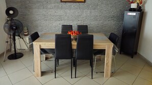 A dining area with a brick wall, a painting, a fan, a cabinet, and a table with chairs. - Quiet and relaxing apartment in Coxyde, 5 minutes walk from the beach (Koksijde)