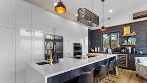 Una cocina moderna con armarios blancos, una isla central, taburetes negros y lámparas colgantes.