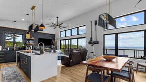 Una cocina moderna con una isla grande, un comedor con mesa de madera y vista al océano.