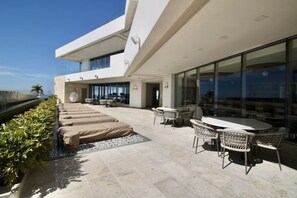 A modern outdoor patio with lounge chairs and a dining area, overlooking a body of water.