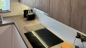 A modern kitchen with wooden panel walls, a black countertop, and a window with blinds.