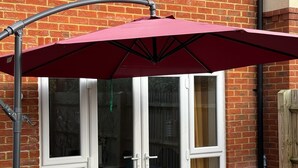 A patio area with a red umbrella, two chairs, and a glass door leading to a room.
