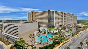 A large hotel with multiple floors, a central courtyard with a swimming pool, and a parking area. - Spacious Ocean View Resort Condo  & 5 Pools (Panama City Beach)