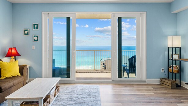 A living room with a view of the ocean through large sliding glass doors. - Spacious Ocean View Resort Condo  & 5 Pools (Panama City Beach)