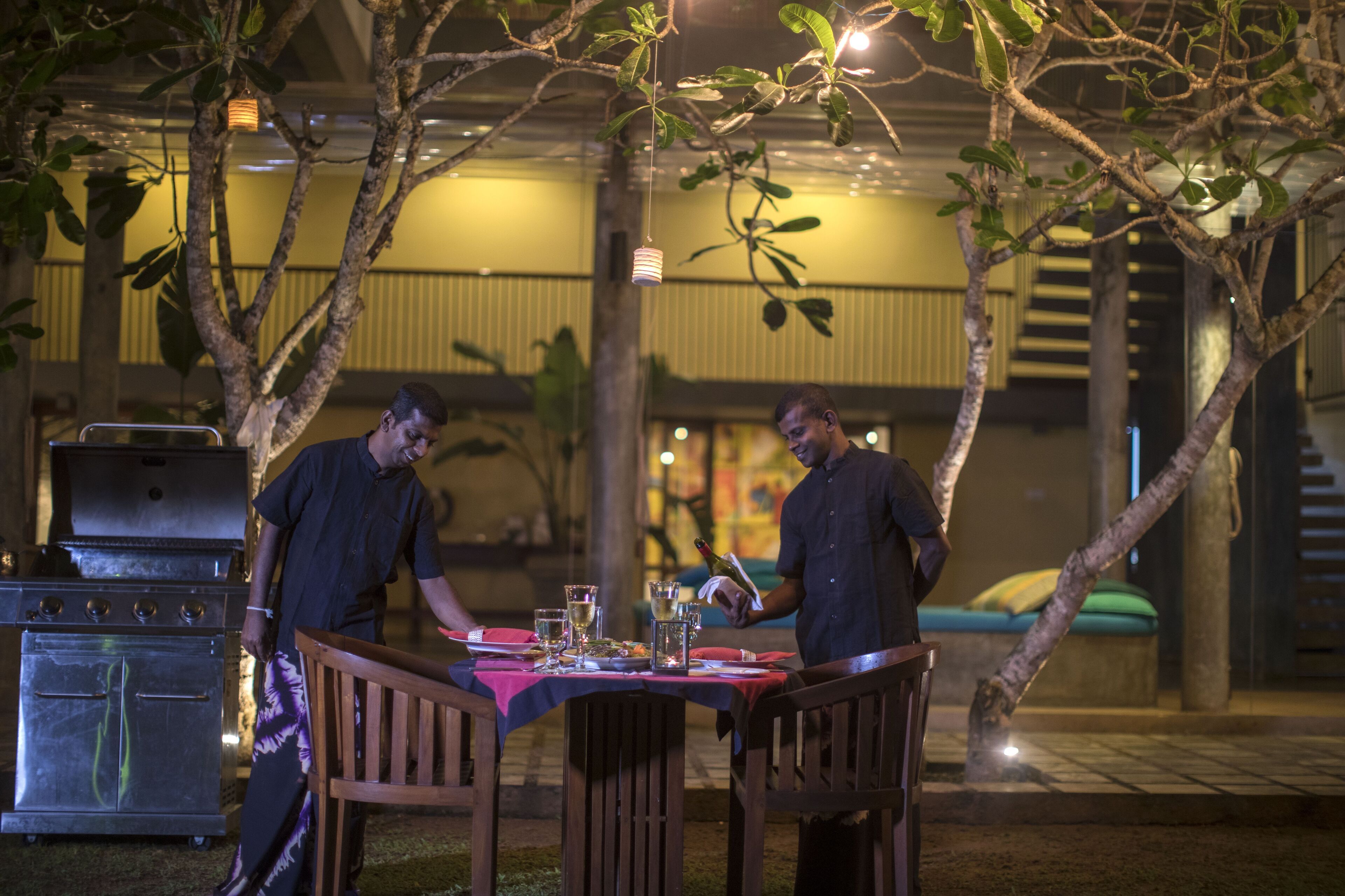 Un área de comedor al aire libre con una mesa lista para dos personas, rodeada de árboles.