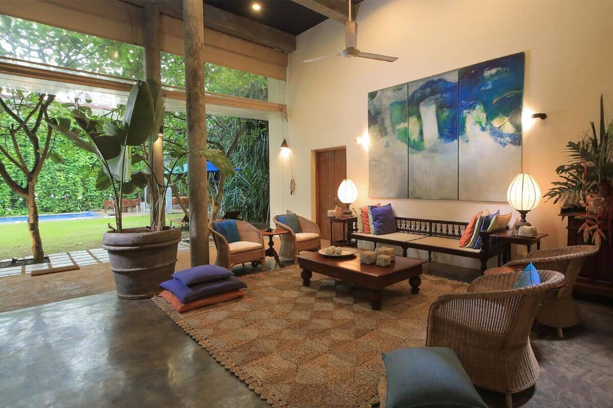 A spacious living area with a large painting, wicker furniture, and a view of greenery outside.