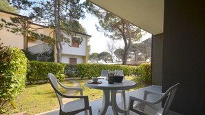 Eine Terrasse mit rundem Tisch und vier Stühlen, umgeben von Grünpflanzen und einem Gebäude im Hintergrund.