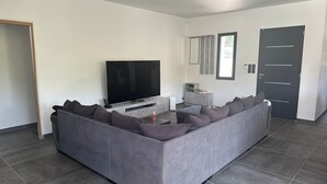 A modern living room with a grey sectional sofa, a flat-screen TV, a small cabinet, and a door. - Villa with private pool in a quiet location 10 min from Avignon (ROCHEFORT DU GARD)