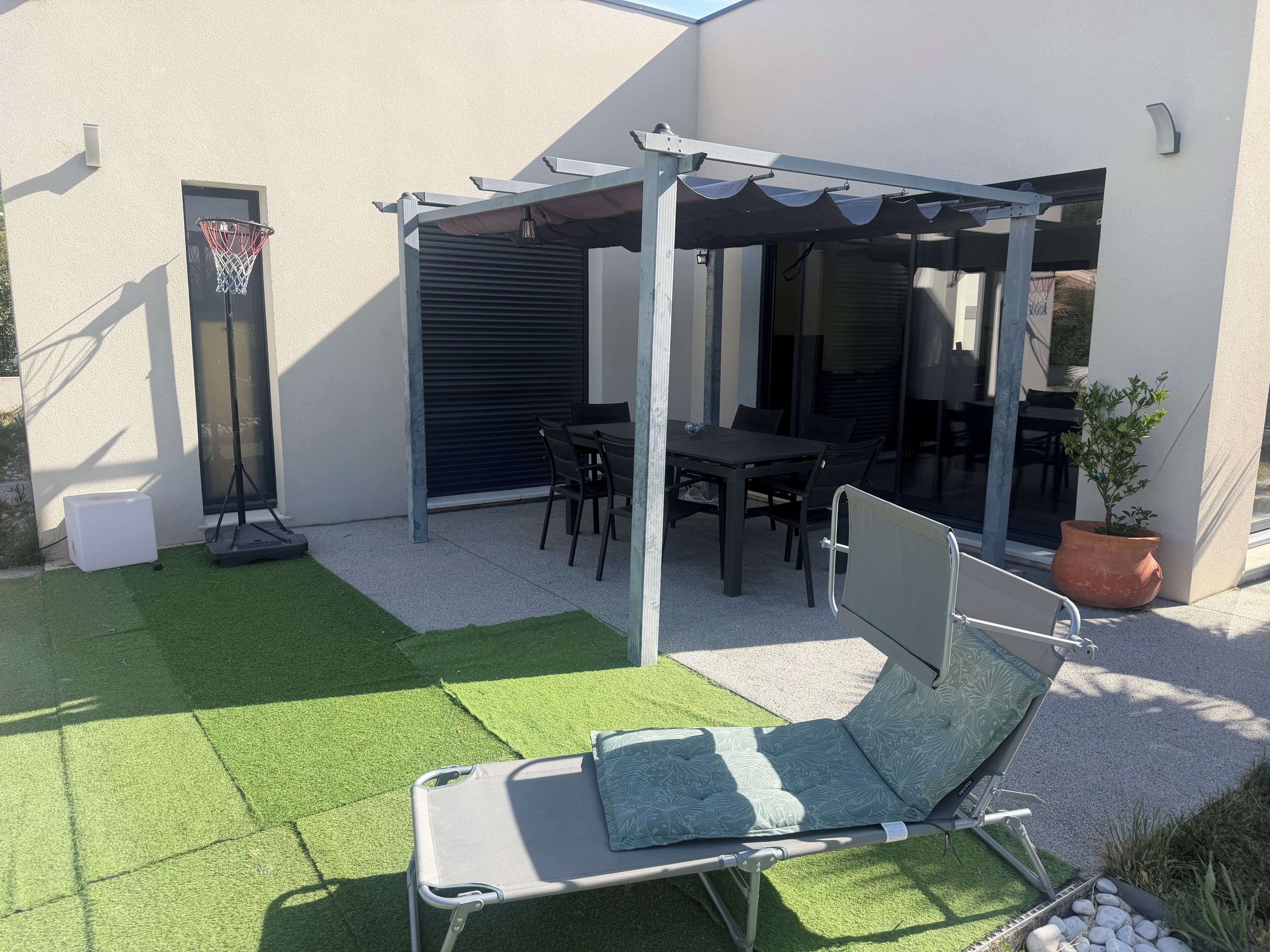 A patio with a table and chairs, a covered seating area, a small garden, and a lounge chair.