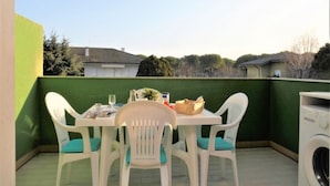 A small outdoor patio with a table and chairs, a washing machine, and a view of houses in the background. - Well furnished three room apartment in Lignano (Lignano Sabbiadoro)