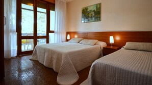 Une chambre d’hôtel avec deux lits, une tête de lit en bois, un tableau au mur et une vue sur l’extérieur, visible à travers une porte vitrée.