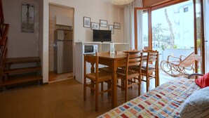 Une pièce compacte comprenant un lit, une table à manger avec des chaises, un coin cuisine et un balcon aménagé avec des meubles en osier.