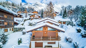 Eine verschneite Berghütte mit mehreren Holzgebäuden, einem zentralen Gebäude mit Balkon und einer verschneiten Landschaft.